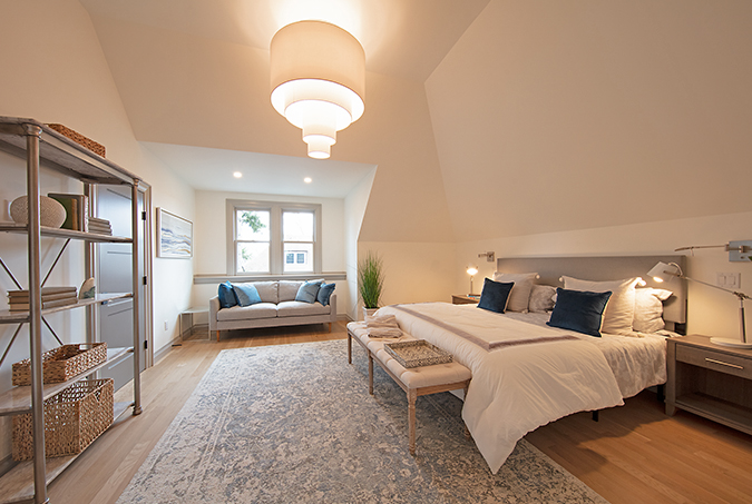 Primary bedroom with custom paneled wall, soft neutral bedding, and daylight from tall windows